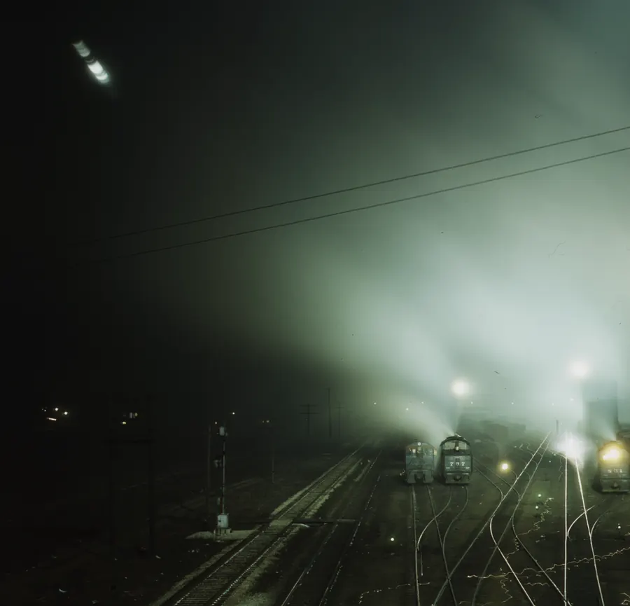 Archival photograph: the Santa Fe railroad yard at Kansas City, Kansas at night, floodlights burning through steam over the classification tracks. Jack Delano for the Office of War Information, March 1943.